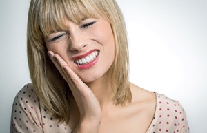 A young female with blonde hair holding her cheek and cringing in pain